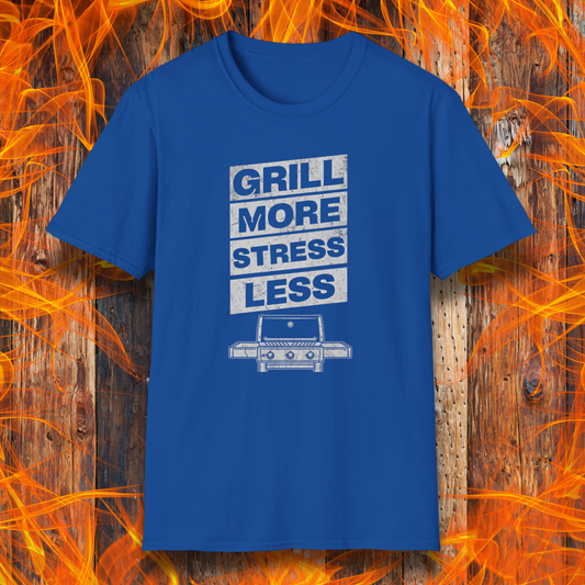 Blue t-shirt with 'Grill More Stress Less' text on a wooden background with flames.
