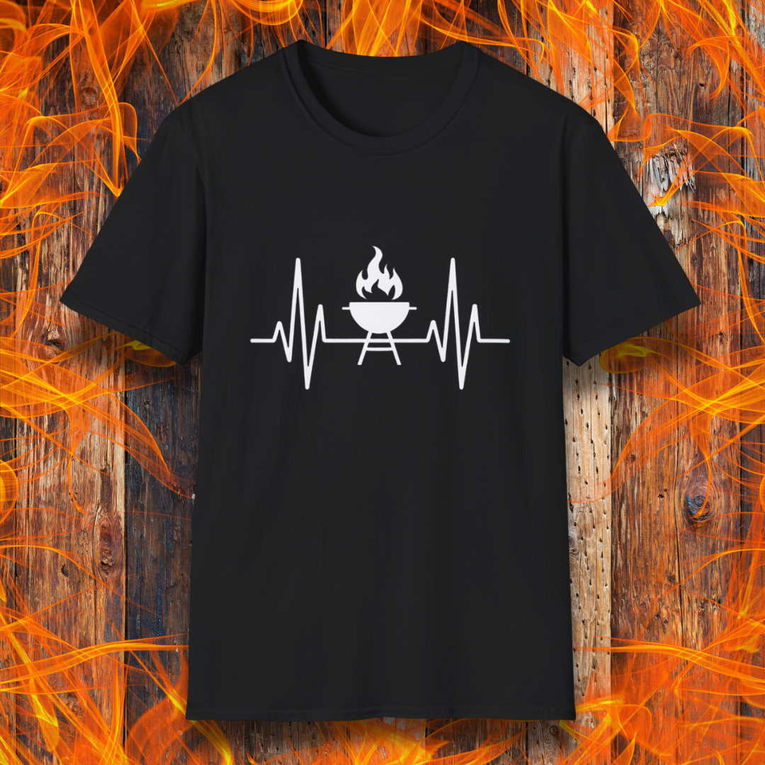 Black T-shirt featuring a minimalist black design of a heartbeat line that transitions into a flaming charcoal grill in the center. The design symbolizes a passion for BBQ, integrating a clean and modern aesthetic. The background consists of a rustic wooden surface with vivid orange flames, enhancing the fiery and grilling-focused theme.