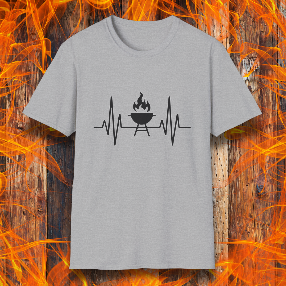 Sport Grey T-shirt featuring a minimalist black design of a heartbeat line that transitions into a flaming charcoal grill in the center. The design symbolizes a passion for BBQ, integrating a clean and modern aesthetic. The background consists of a rustic wooden surface with vivid orange flames, enhancing the fiery and grilling-focused theme.