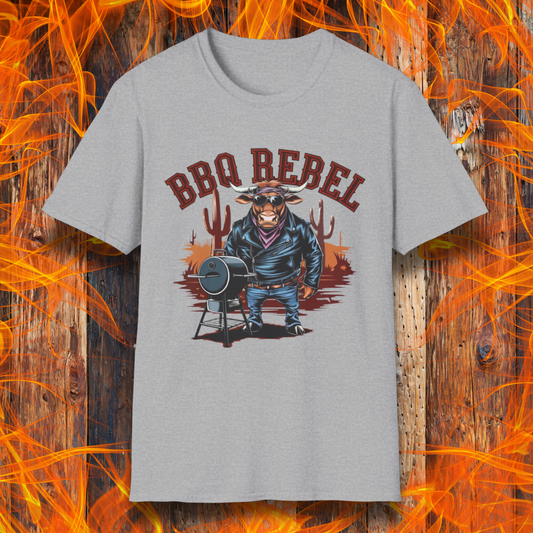 Sport Grey T-shirt featuring a bold and rebellious BBQ-themed design. The centerpiece is an anthropomorphic bull dressed like a biker, wearing a black leather jacket, blue jeans, and a red bandana, exuding a tough and confident attitude. He stands next to a classic barrel-style smoker. The background includes red flames and grill forks, adding to the edgy, fiery vibe. Above the character, "BBQ REBEL" is displayed in bold, vintage-style red lettering.