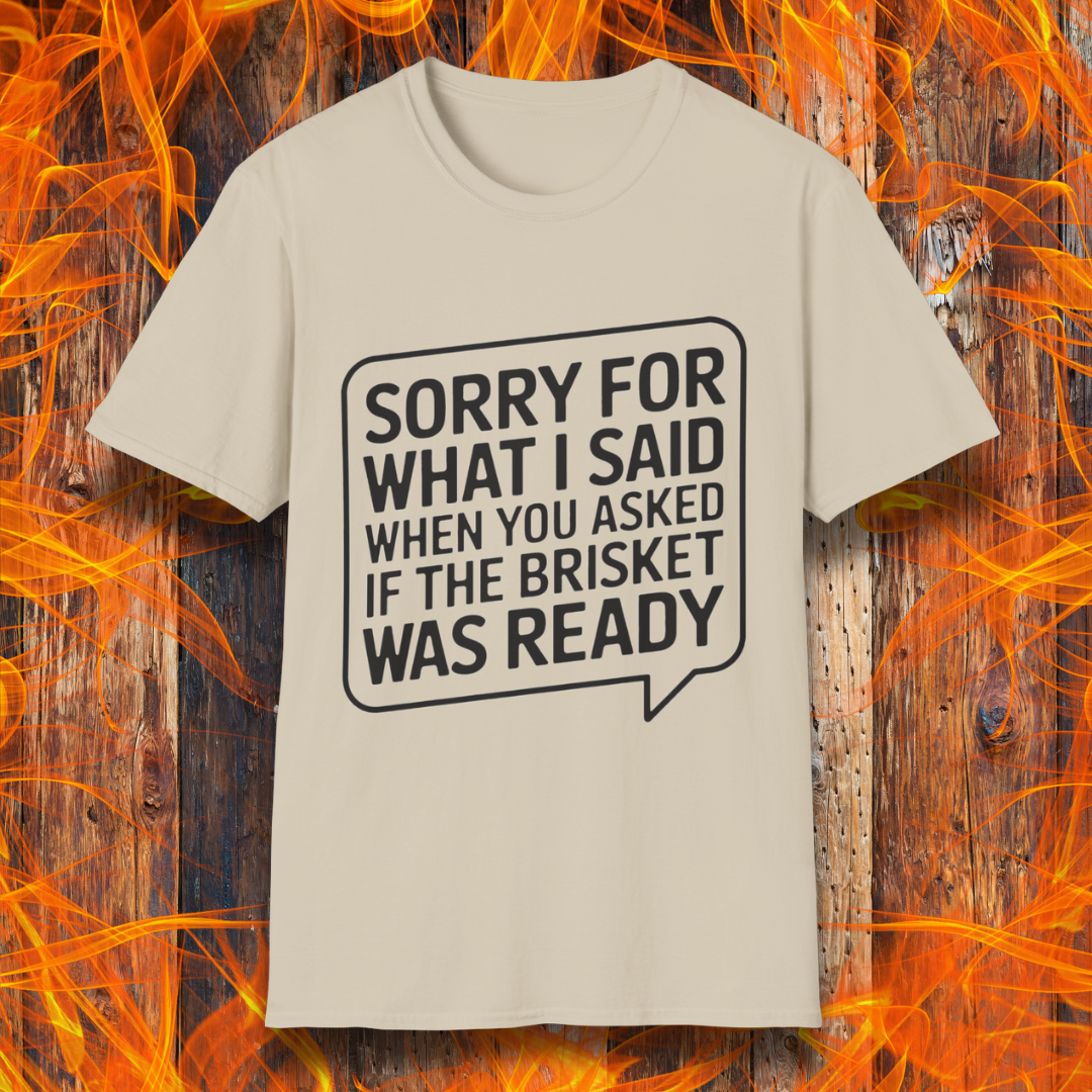 Sand T-shirt with bold white text inside a speech bubble that reads, "Sorry for what I said when you asked if the brisket was ready." A fun and relatable design for BBQ lovers and pitmasters.