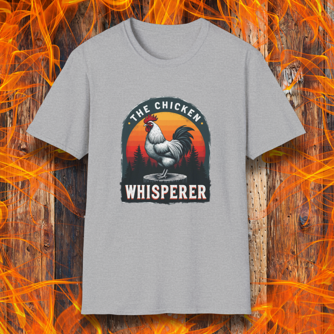 Sport Grey T-shirt featuring a bold design with a proud rooster standing on a wooden stump. The rooster is framed by an arched emblem with a scenic sunset gradient in orange, red, and yellow hues, along with a silhouette of pine trees in the background. The text "THE CHICKEN WHISPERER" is displayed prominently, giving the design a humorous and rustic feel, perfect for backyard BBQ enthusiasts and poultry lovers.