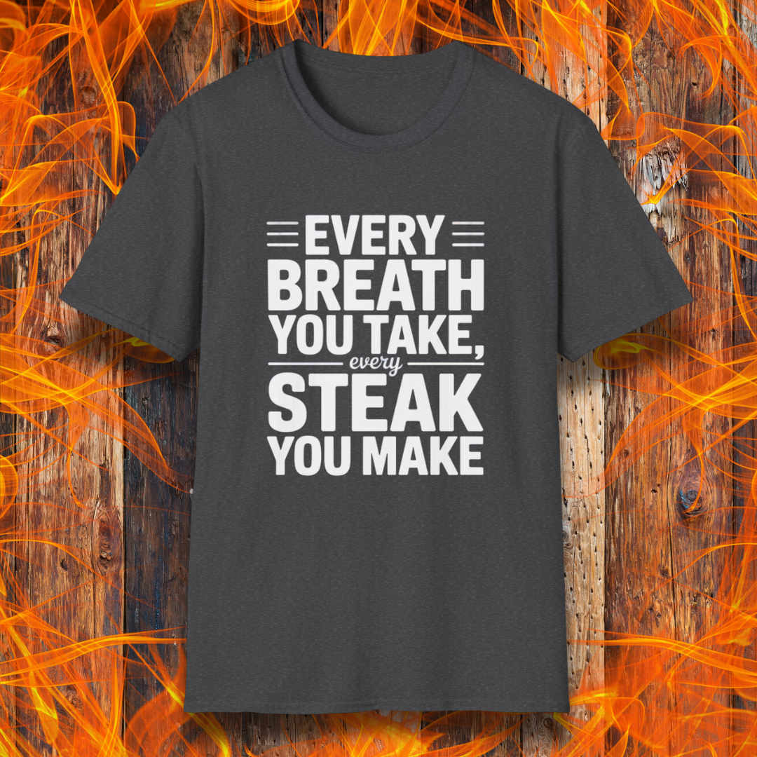 Dark Heather T-shirt with bold white text that reads "Every Breath You Take, Every Steak You Make," displayed over a rustic wood and flame background — a humorous grilling shirt perfect for steak fans.