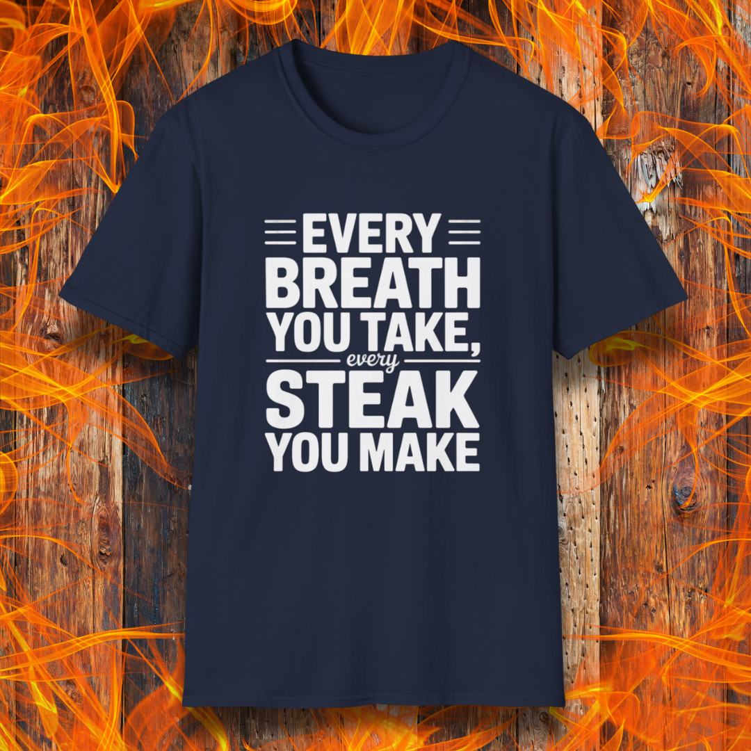 Navy T-shirt with bold white text that reads "Every Breath You Take, Every Steak You Make," displayed over a rustic wood and flame background — a humorous grilling shirt perfect for steak fans.