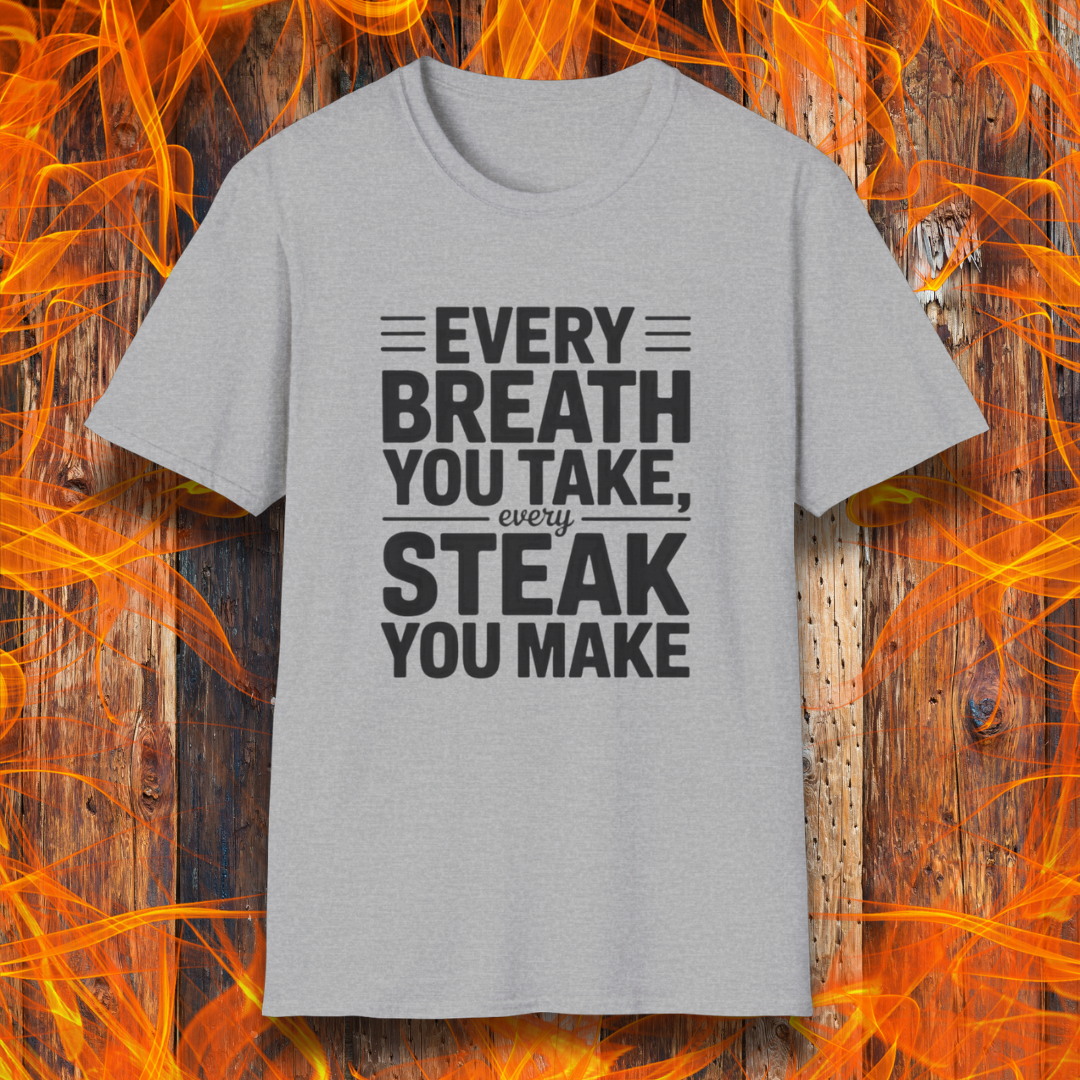 Sport Grey T-shirt with bold white text that reads "Every Breath You Take, Every Steak You Make," displayed over a rustic wood and flame background — a humorous grilling shirt perfect for steak fans.