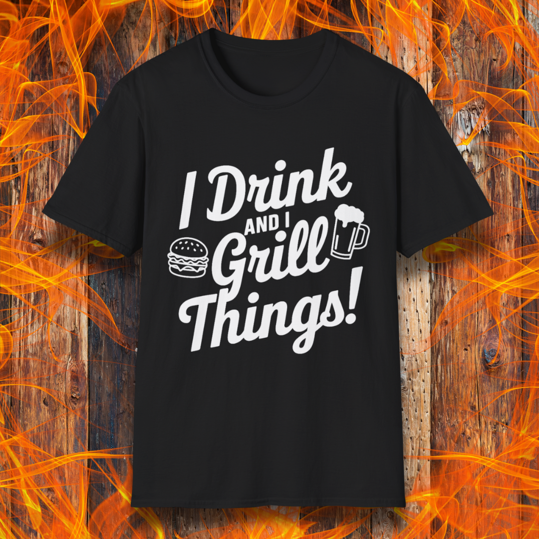 BlackT-shirt featuring a bold, black text design that reads, "I Drink and I Grill Things!" in a playful, script-style font. The design includes small illustrations of a burger and a frothy beer mug, emphasizing a fun and laid-back grilling theme. The background showcases a rustic wooden surface with bright orange flames, enhancing the fiery BBQ aesthetic.
