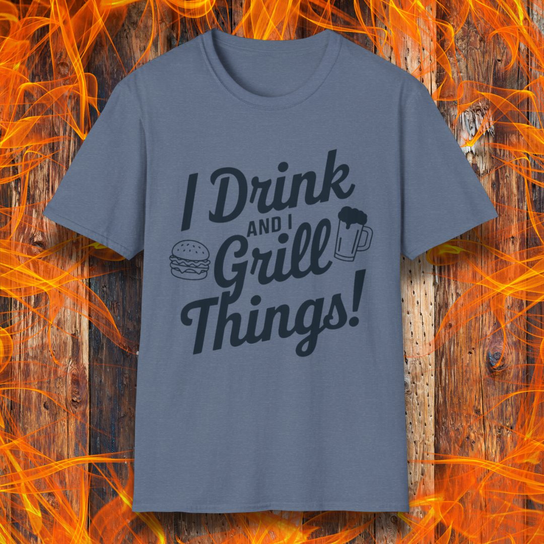 Heather Indigo T-shirt featuring a bold, black text design that reads, "I Drink and I Grill Things!" in a playful, script-style font. The design includes small illustrations of a burger and a frothy beer mug, emphasizing a fun and laid-back grilling theme. The background showcases a rustic wooden surface with bright orange flames, enhancing the fiery BBQ aesthetic.