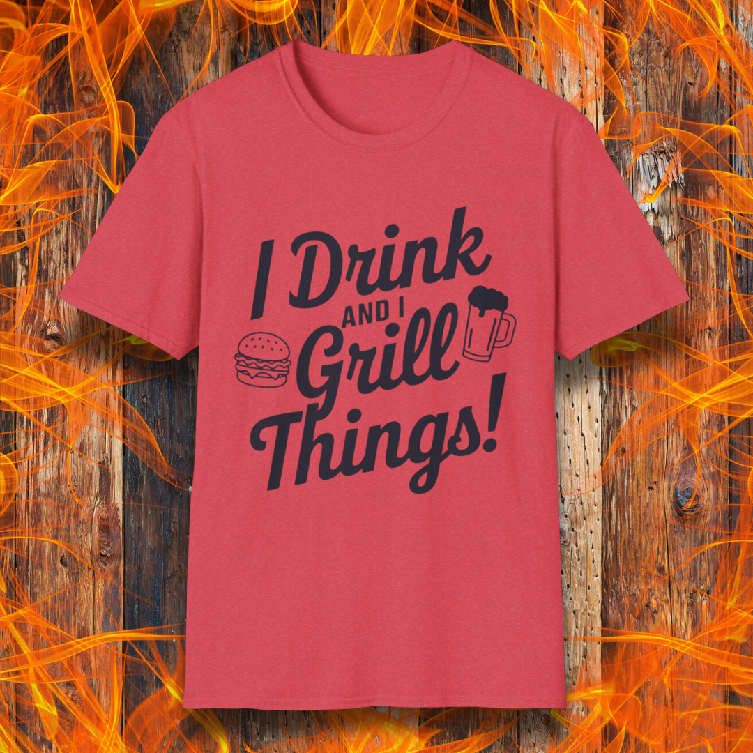 Heather Red T-shirt featuring a bold, black text design that reads, "I Drink and I Grill Things!" in a playful, script-style font. The design includes small illustrations of a burger and a frothy beer mug, emphasizing a fun and laid-back grilling theme. The background showcases a rustic wooden surface with bright orange flames, enhancing the fiery BBQ aesthetic.