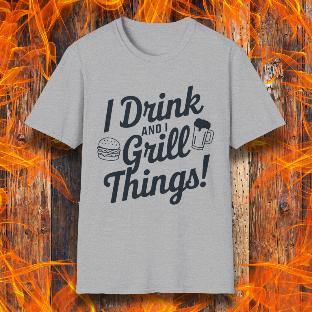 Sport Grey T-shirt featuring a bold, black text design that reads, "I Drink and I Grill Things!" in a playful, script-style font. The design includes small illustrations of a burger and a frothy beer mug, emphasizing a fun and laid-back grilling theme. The background showcases a rustic wooden surface with bright orange flames, enhancing the fiery BBQ aesthetic.