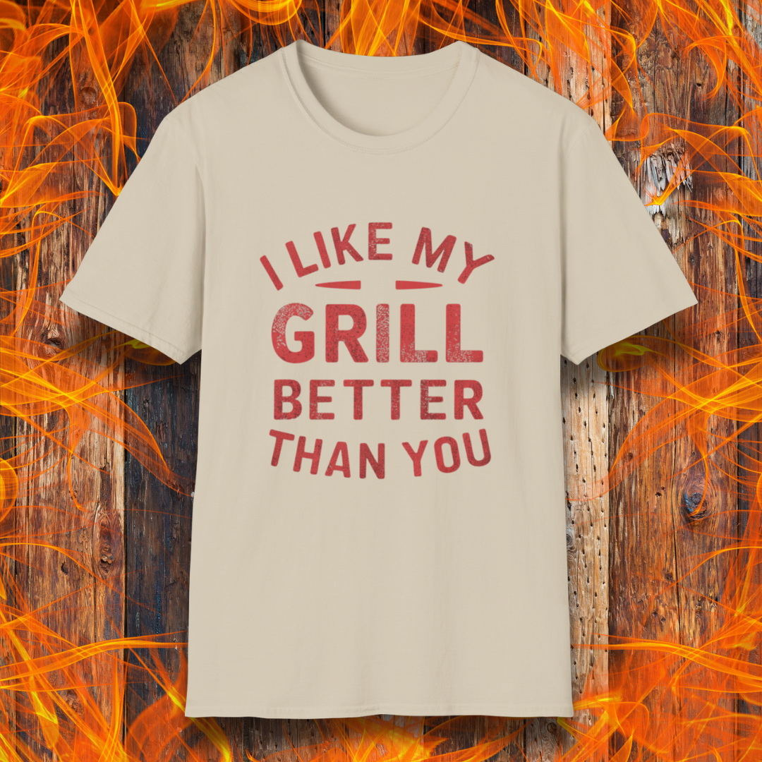 Sand T-shirt with a bold and humorous BBQ-themed design. The red distressed-style text reads 'I Like My Grill Better Than You' in an arched layout, perfect for grill masters who take their barbecue seriously. A fun and stylish shirt for BBQ enthusiasts."