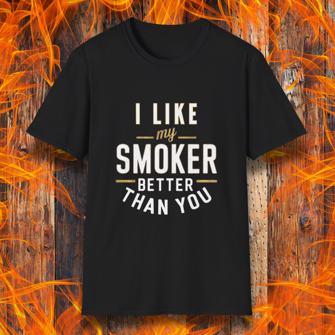 Black T-shirt featuring a witty BBQ-themed design. The bold text reads 'I Like My Smoker Better Than You' in a mix of white and gold lettering, with decorative lines adding emphasis. A perfect shirt for grill masters and smoking enthusiasts with a sense of humor.