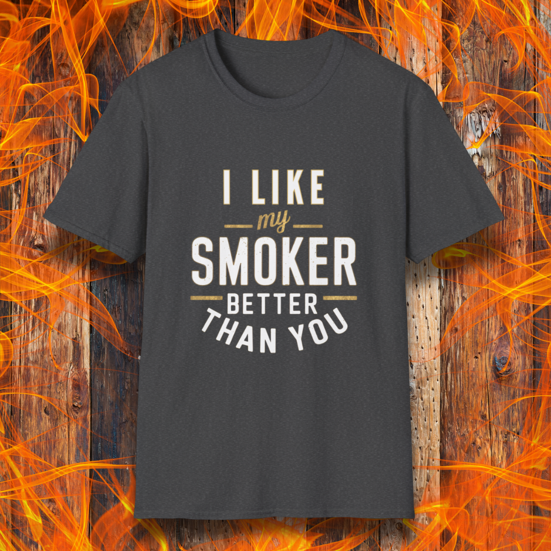 Dark Heather T-shirt featuring a witty BBQ-themed design. The bold text reads 'I Like My Smoker Better Than You' in a mix of white and gold lettering, with decorative lines adding emphasis. A perfect shirt for grill masters and smoking enthusiasts with a sense of humor.