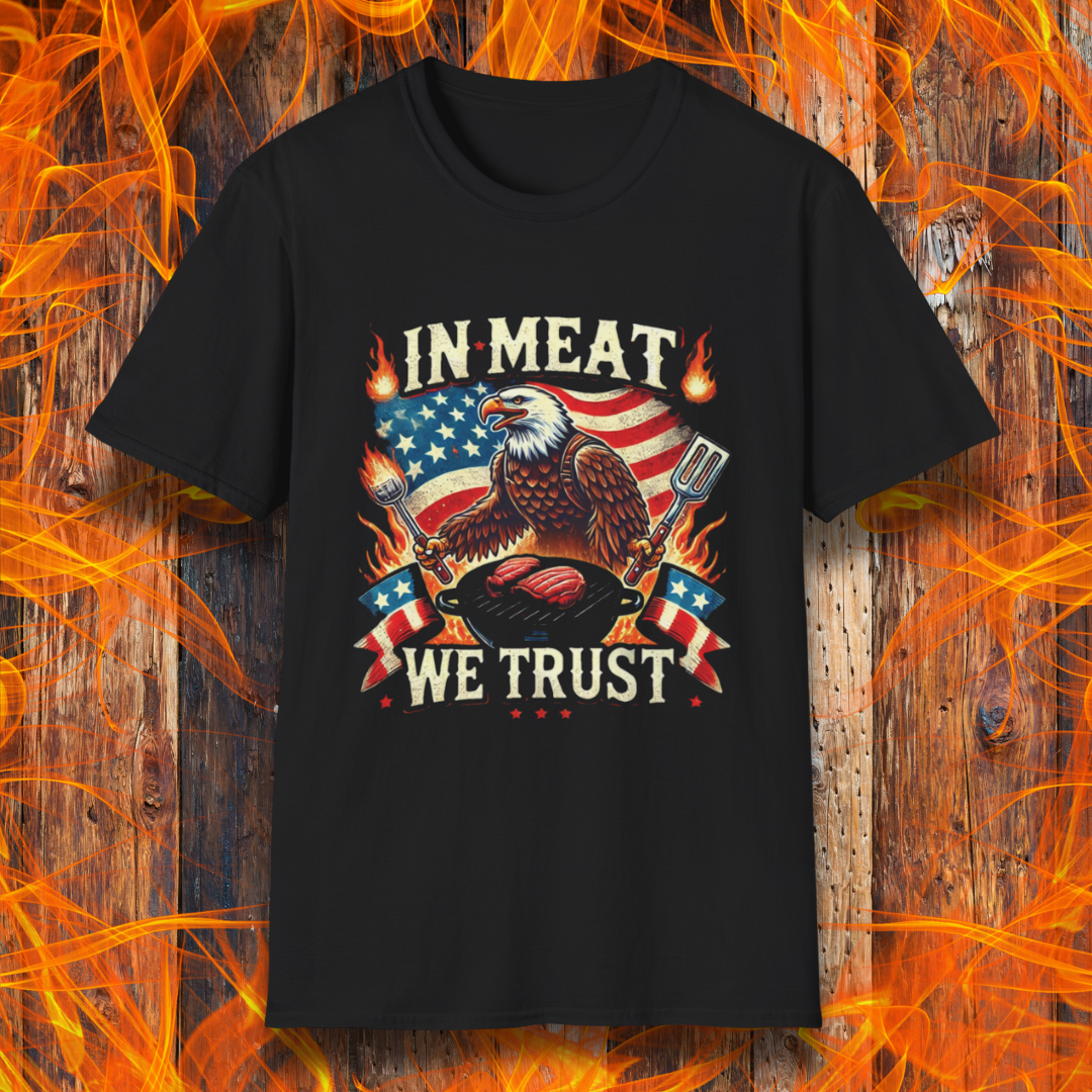 Black BBQ-themed T-shirt featuring a bold patriotic design with an American flag, a fierce bald eagle holding grilling utensils, flames, and the phrase 'In Meat We Trust' in vintage-style lettering.