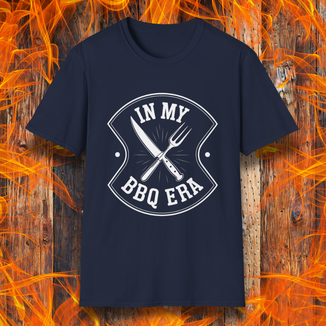 Navy T-shirt featuring a bold black design with the phrase "IN MY BBQ ERA" inside a shield-like emblem. At the center of the emblem, there is a crossed knife and grilling fork, symbolizing BBQ culture. The background showcases a rustic wooden texture with bright orange flames, adding a fiery and intense grilling aesthetic.