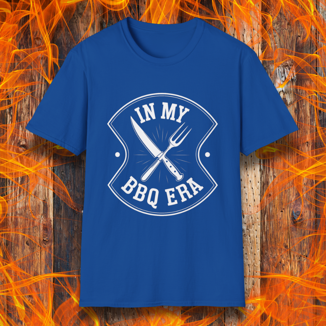 Royal Blue T-shirt featuring a bold black design with the phrase "IN MY BBQ ERA" inside a shield-like emblem. At the center of the emblem, there is a crossed knife and grilling fork, symbolizing BBQ culture. The background showcases a rustic wooden texture with bright orange flames, adding a fiery and intense grilling aesthetic.