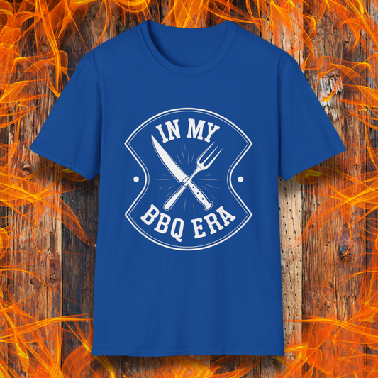 Royal Blue T-shirt featuring a bold black design with the phrase "IN MY BBQ ERA" inside a shield-like emblem. At the center of the emblem, there is a crossed knife and grilling fork, symbolizing BBQ culture. The background showcases a rustic wooden texture with bright orange flames, adding a fiery and intense grilling aesthetic.