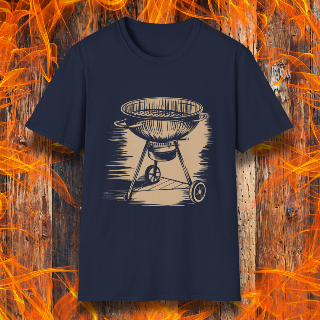 Navy T-shirt featuring a vintage-style beige sketch of a classic charcoal kettle grill. The illustration has a hand-drawn, rustic look with shading lines that add depth and texture. The background consists of a wooden surface with bright orange flames, enhancing the fiery BBQ theme.