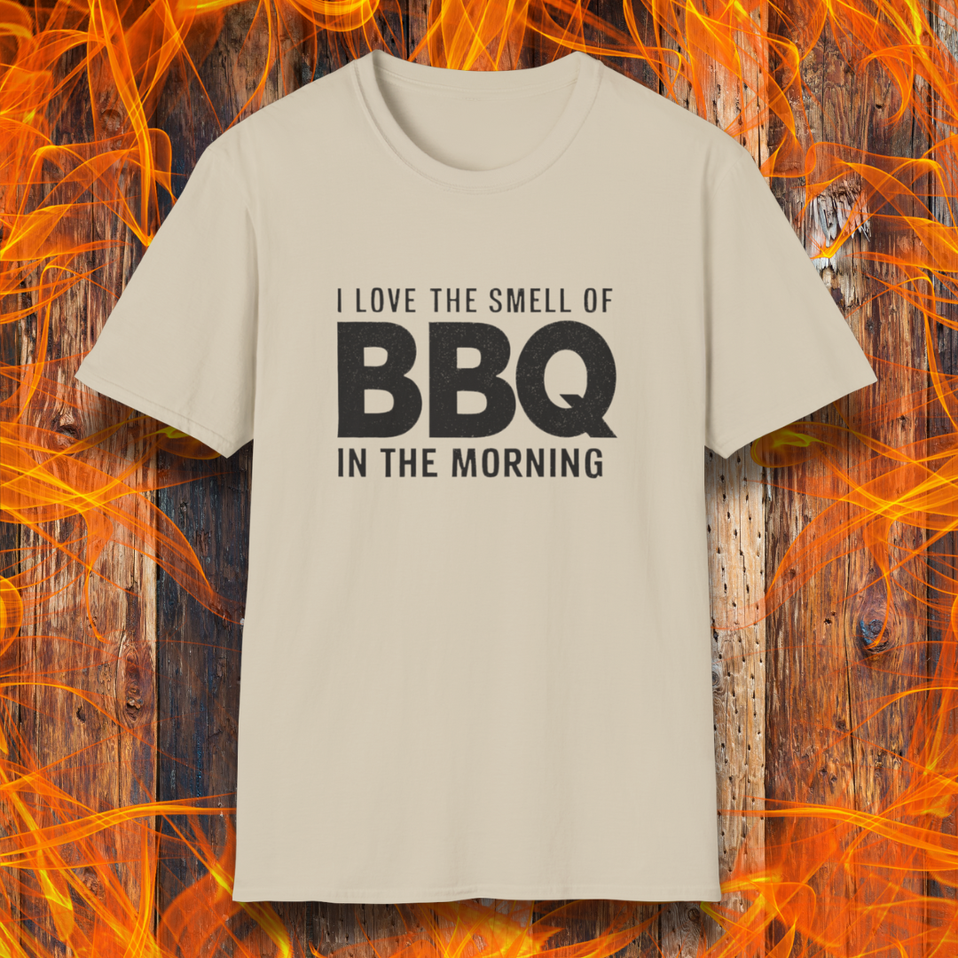 Sand t-shirt with the phrase 'I Love the Smell of BBQ in the Morning' in bold white text, displayed against a fiery wooden background