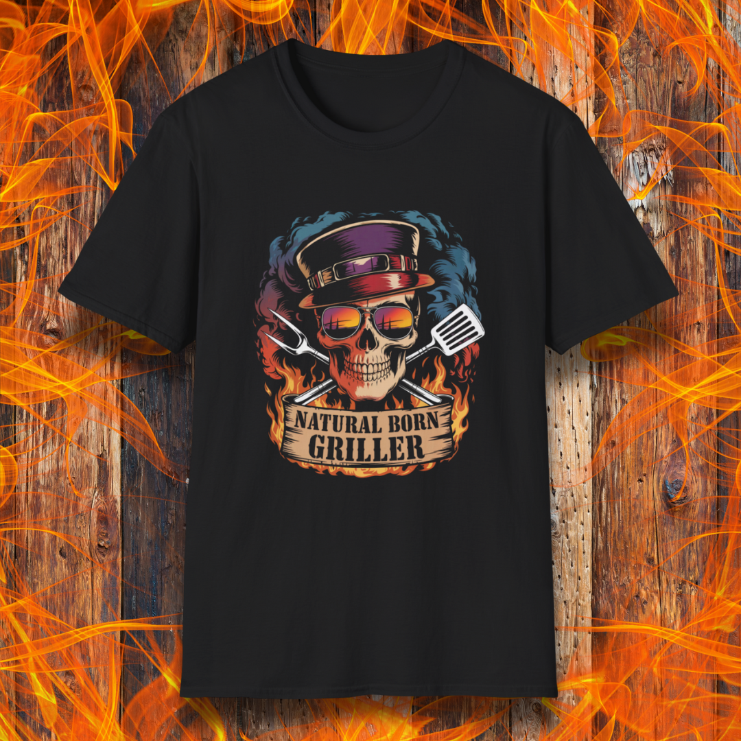 Black T-shirt featuring a flaming skull in sunglasses and a top hat, flanked by grilling tools with the phrase "Natural Born Griller" — set against a rustic wood and flame background, perfect for bold BBQ enthusiasts.