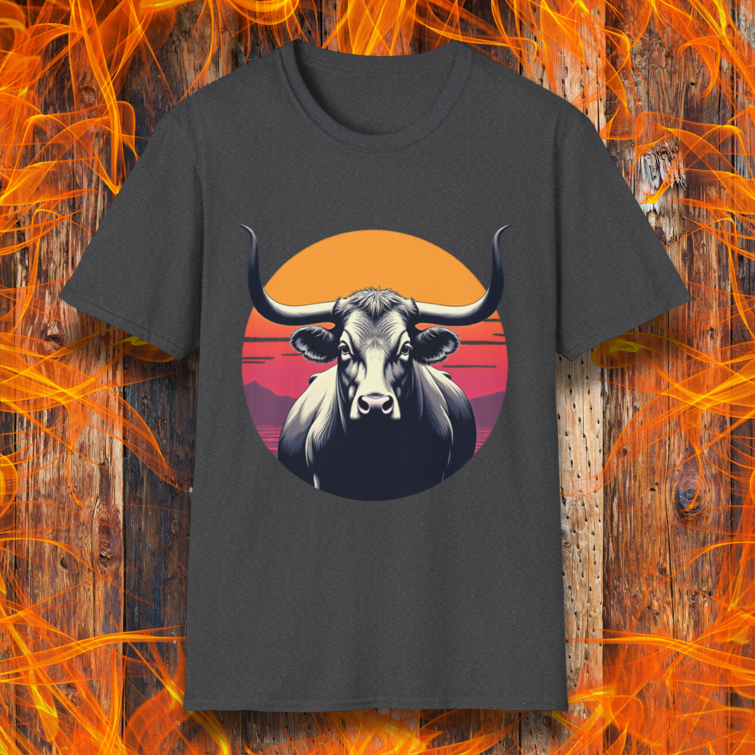 Dark Heather T-shirt featuring a striking design of a longhorn bull staring forward with an intense gaze. The bull is set against a circular backdrop of a sunset with warm orange, red, and pink hues, along with silhouetted mountains in the background. The design conveys strength, confidence, and a bold Western aesthetic, appealing to BBQ and cattle enthusiasts.