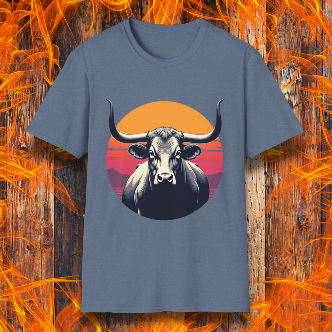 Heather Indigo T-shirt featuring a striking design of a longhorn bull staring forward with an intense gaze. The bull is set against a circular backdrop of a sunset with warm orange, red, and pink hues, along with silhouetted mountains in the background. The design conveys strength, confidence, and a bold Western aesthetic, appealing to BBQ and cattle enthusiasts.