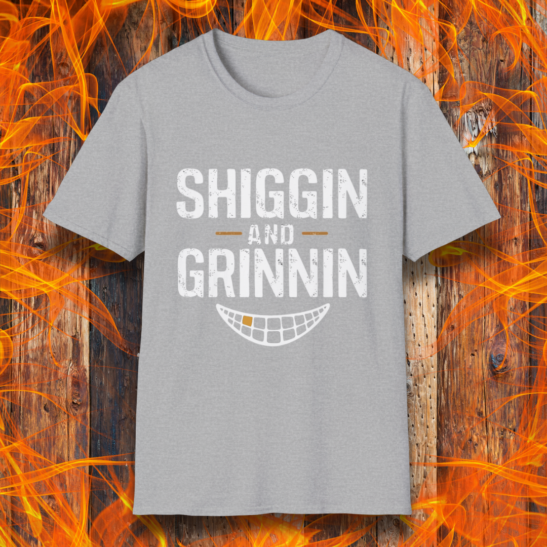 Sport Grey T-shirt featuring the phrase 'Shiggin and Grinnin' in bold, distressed white lettering. Below the text is a stylized smiling grill grate graphic. The design is set against a rustic wooden background with flames surrounding the edges, giving it a fiery barbecue-themed look.