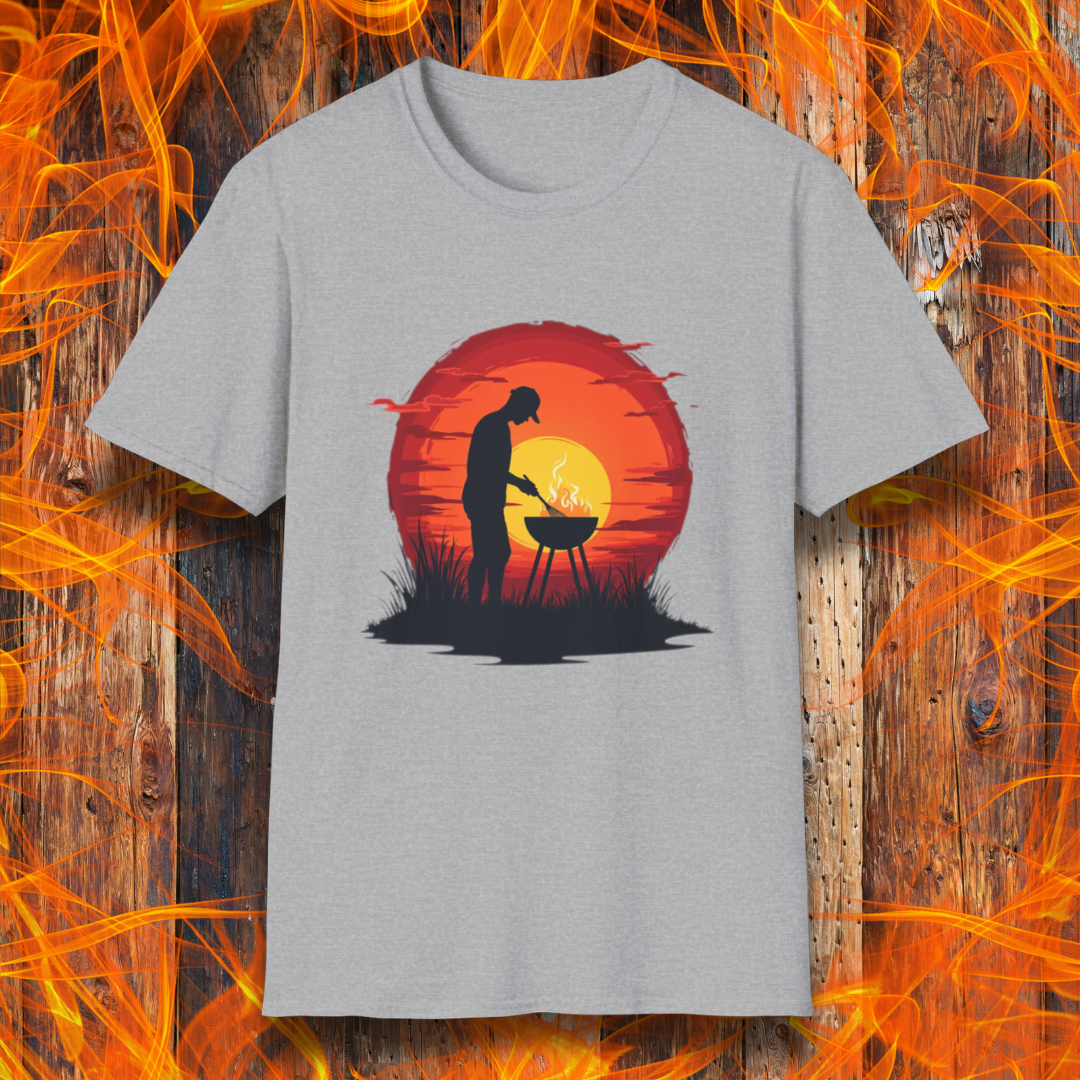 Sport Grey T-shirt featuring a vibrant design of a silhouetted man grilling in front of a large, glowing sunset. The sunset has warm hues of red, orange, and yellow, creating a striking contrast against the dark background. The scene is framed with grass and subtle clouds, giving it an outdoorsy, serene BBQ vibe.
