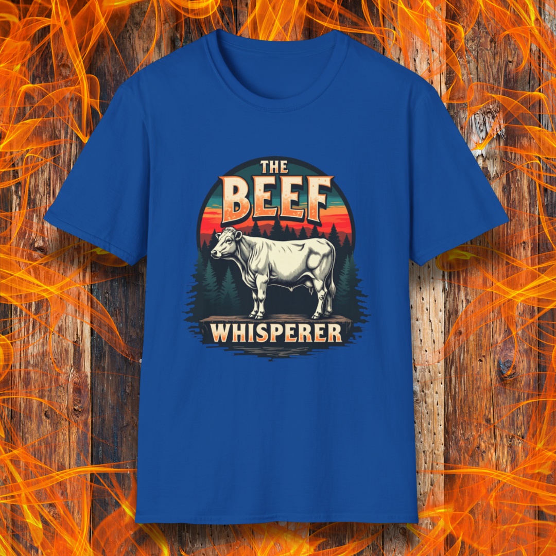 Royal Blue T-shirt featuring a bold design with the words "The Beef Whisperer" in a vintage western-style font. Above the text, a detailed illustration of a cow stands on a patch of ground, framed by a scenic forest and a sunset with deep orange and red hues. The design has a rustic, outdoorsy feel, appealing to BBQ lovers and beef enthusiasts.