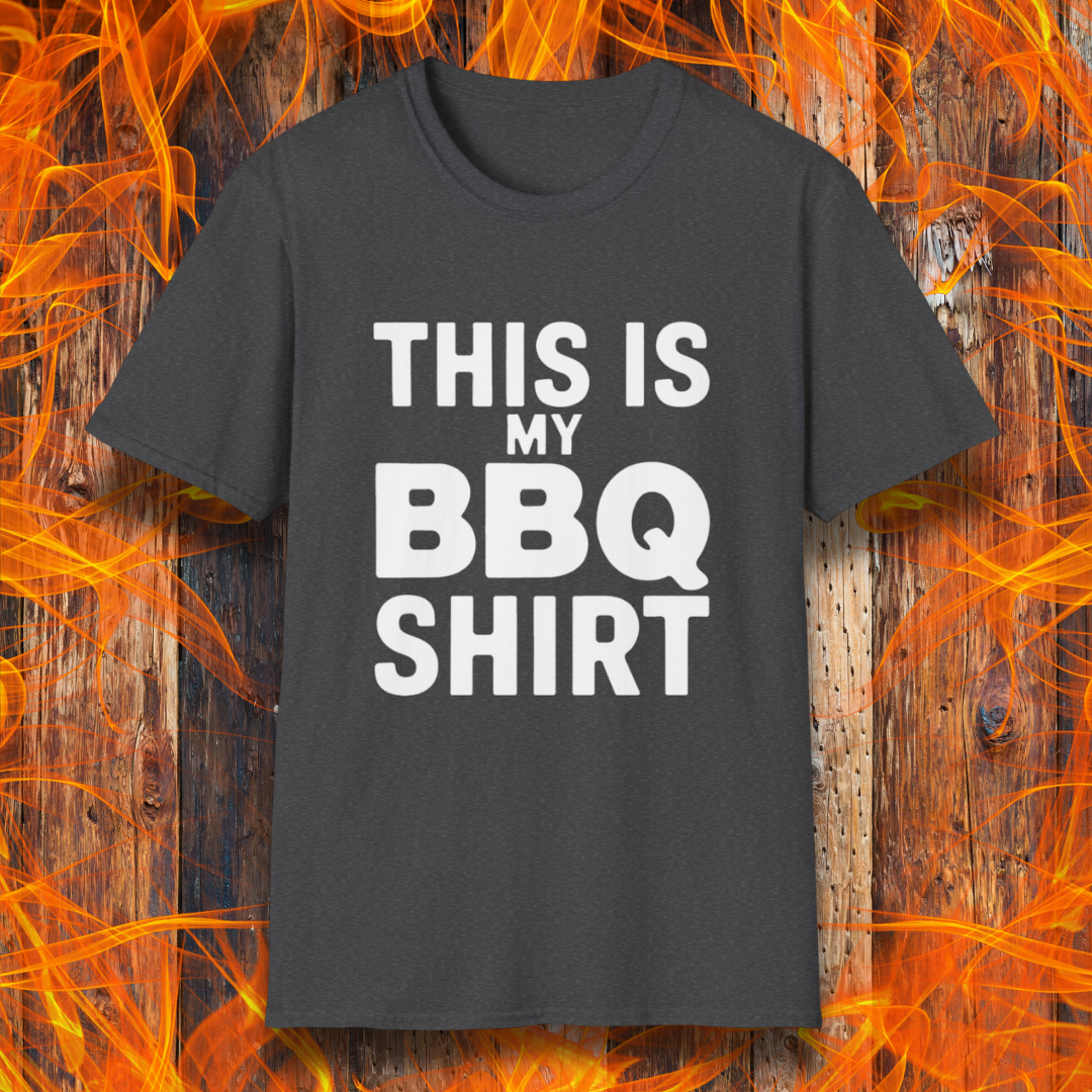Dark Heather T-shirt with bold white text that reads "THIS IS MY BBQ SHIRT." The shirt is displayed against a fiery wooden background, reinforcing its BBQ and grilling theme.
