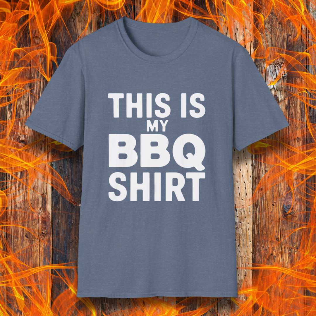 Heather Indigo T-shirt with bold white text that reads "THIS IS MY BBQ SHIRT." The shirt is displayed against a fiery wooden background, reinforcing its BBQ and grilling theme.