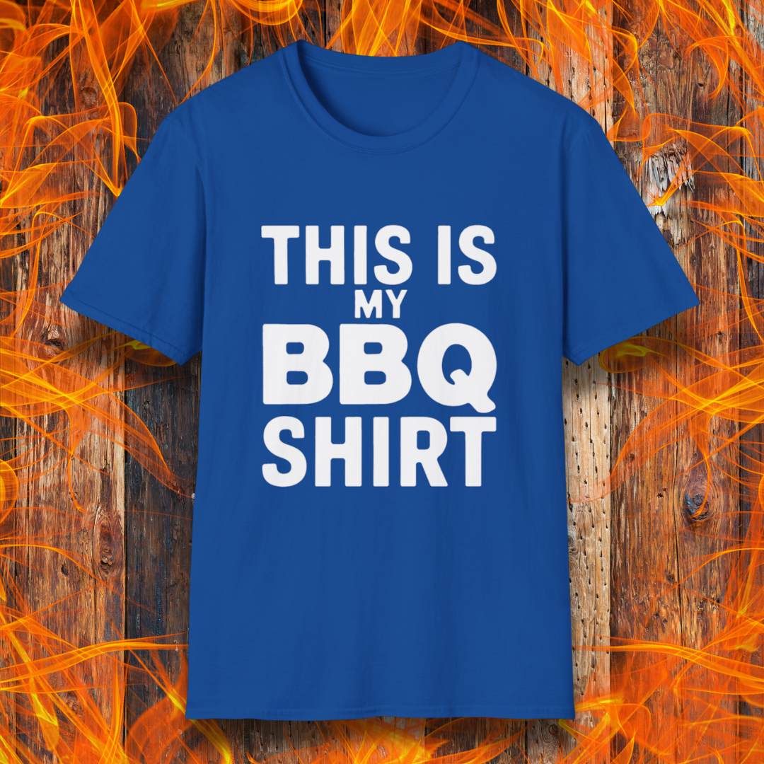 Royal Blue T-shirt with bold white text that reads "THIS IS MY BBQ SHIRT." The shirt is displayed against a fiery wooden background, reinforcing its BBQ and grilling theme.