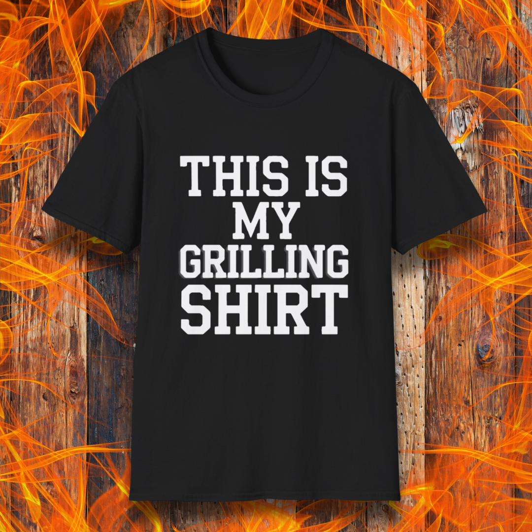 Black T-shirt with bold white text that reads "THIS IS MY GRILLING SHIRT." The shirt is displayed against a fiery wooden background, emphasizing its BBQ and grilling theme.