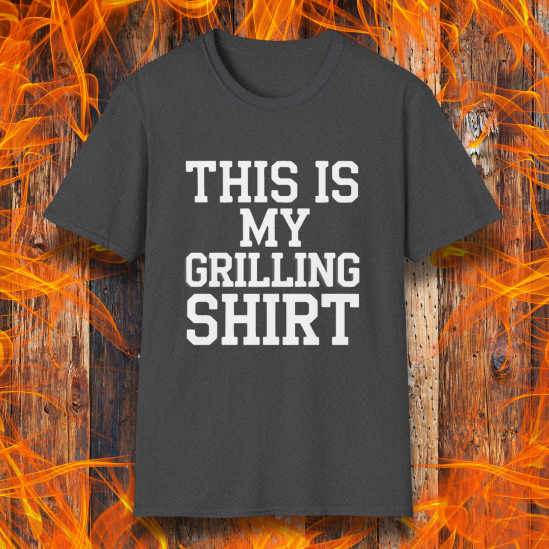 Dark Heather T-shirt with bold white text that reads "THIS IS MY GRILLING SHIRT." The shirt is displayed against a fiery wooden background, emphasizing its BBQ and grilling theme.