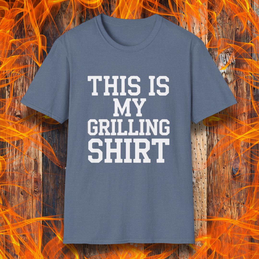 Heather Indigo T-shirt with bold white text that reads "THIS IS MY GRILLING SHIRT." The shirt is displayed against a fiery wooden background, emphasizing its BBQ and grilling theme.