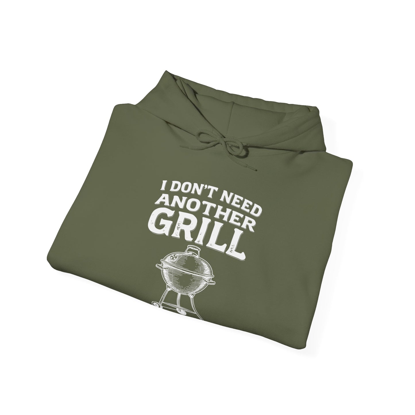 Folded olive green hoodie with white text "I don't need another grill said no guy ever" and graphic on a white background