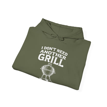 Folded olive green hoodie with white text "I don't need another grill said no guy ever" and graphic on a white background