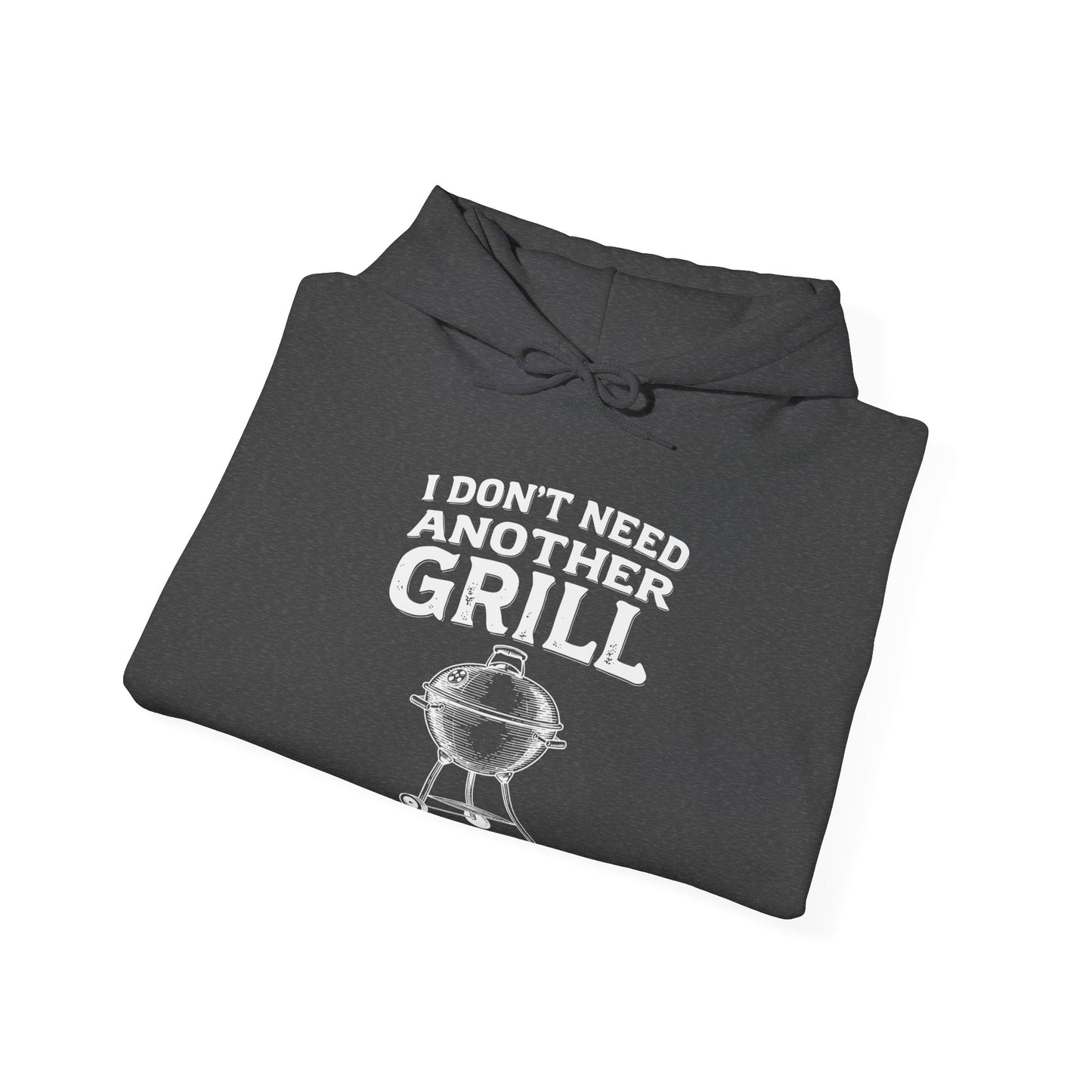 Folded dark gray hoodie with white text "I don't need another grill said no guy ever" and graphic on a white background
