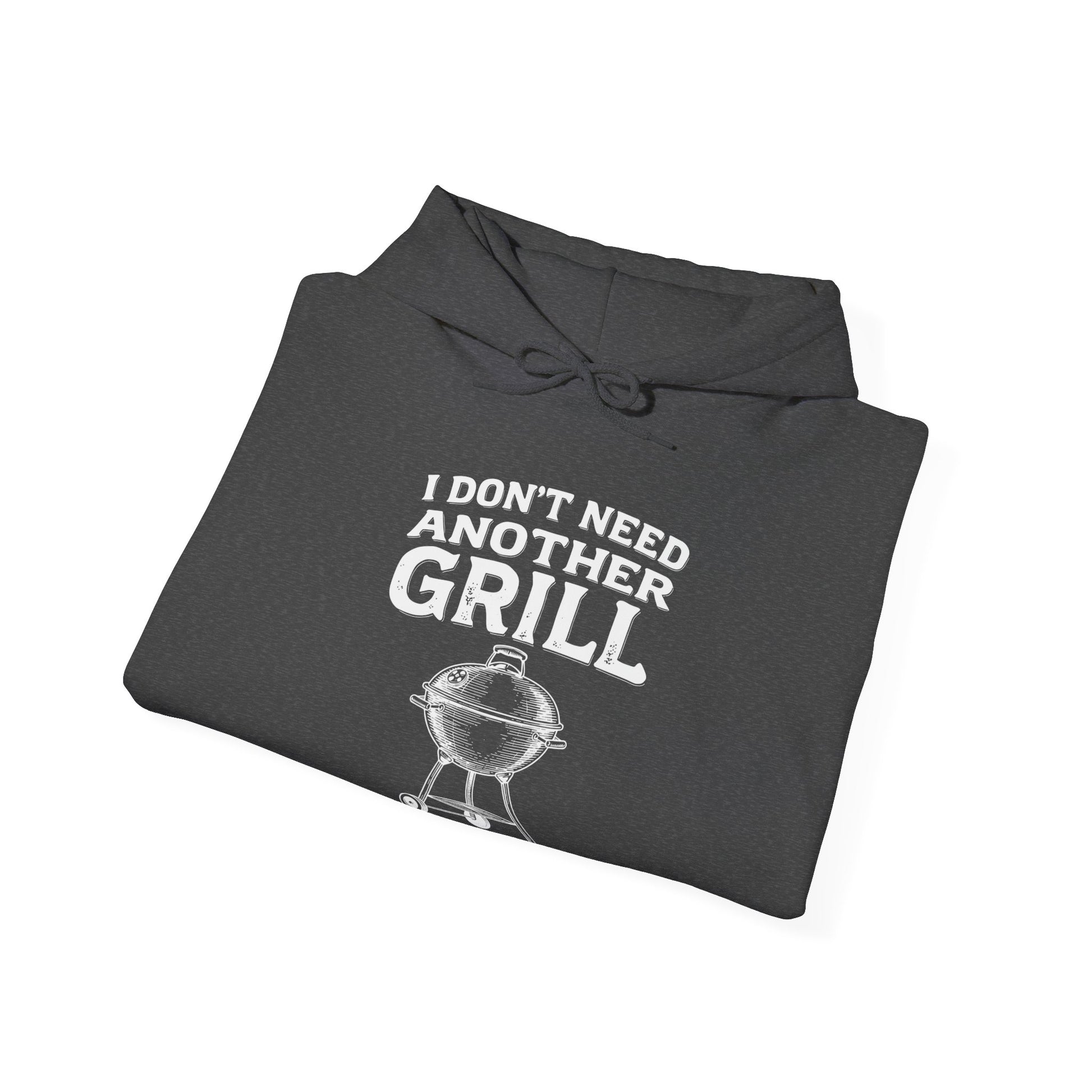 Folded dark gray hoodie with white text "I don't need another grill said no guy ever" and graphic on a white background