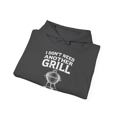 Folded dark gray hoodie with white text "I don't need another grill said no guy ever" and graphic on a white background