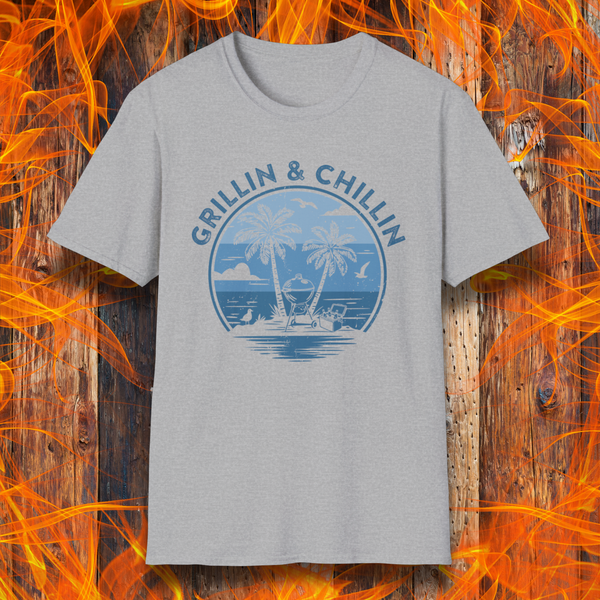 Gray t-shirt with 'Grillin & Chillin' graphic design on a wooden background with flames.
