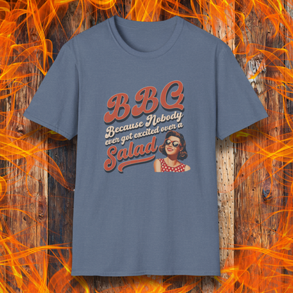 Blue t-shirt with 'BBQ because nobody ever got excited over a salad' text and graphic on a wooden background with flames.