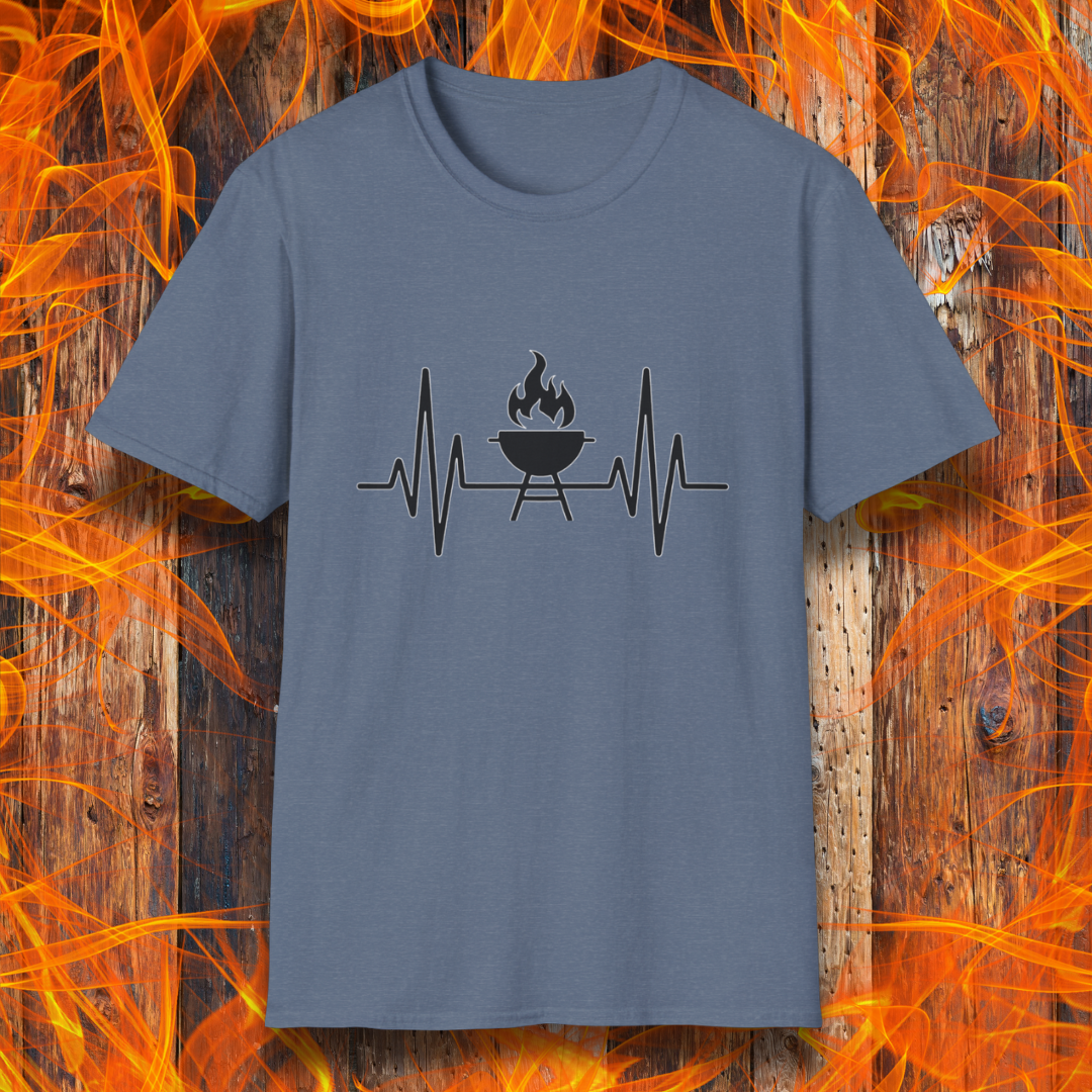 Heather Indigo T-shirt featuring a minimalist black design of a heartbeat line that transitions into a flaming charcoal grill in the center. The design symbolizes a passion for BBQ, integrating a clean and modern aesthetic. The background consists of a rustic wooden surface with vivid orange flames, enhancing the fiery and grilling-focused theme.
