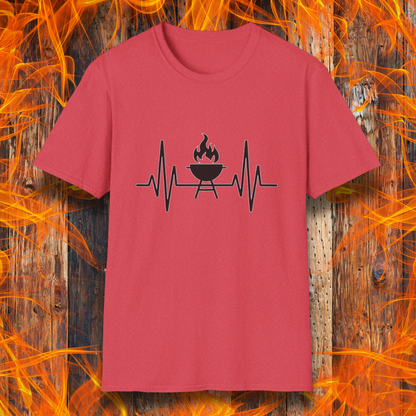 Heather Red T-shirt featuring a minimalist black design of a heartbeat line that transitions into a flaming charcoal grill in the center. The design symbolizes a passion for BBQ, integrating a clean and modern aesthetic. The background consists of a rustic wooden surface with vivid orange flames, enhancing the fiery and grilling-focused theme.