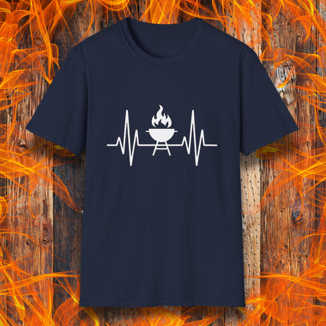 Navy T-shirt featuring a minimalist black design of a heartbeat line that transitions into a flaming charcoal grill in the center. The design symbolizes a passion for BBQ, integrating a clean and modern aesthetic. The background consists of a rustic wooden surface with vivid orange flames, enhancing the fiery and grilling-focused theme.