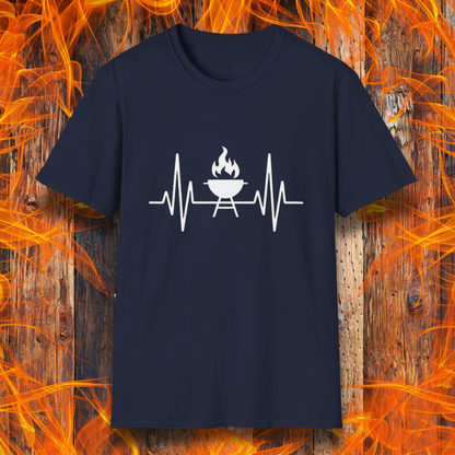 Navy T-shirt featuring a minimalist black design of a heartbeat line that transitions into a flaming charcoal grill in the center. The design symbolizes a passion for BBQ, integrating a clean and modern aesthetic. The background consists of a rustic wooden surface with vivid orange flames, enhancing the fiery and grilling-focused theme.