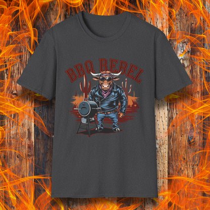 Dark Heather T-shirt featuring a bold and rebellious BBQ-themed design. The centerpiece is an anthropomorphic bull dressed like a biker, wearing a black leather jacket, blue jeans, and a red bandana, exuding a tough and confident attitude. He stands next to a classic barrel-style smoker. The background includes red flames and grill forks, adding to the edgy, fiery vibe. Above the character, "BBQ REBEL" is displayed in bold, vintage-style red lettering.  