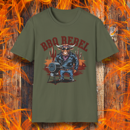 Military Green T-shirt featuring a bold and rebellious BBQ-themed design. The centerpiece is an anthropomorphic bull dressed like a biker, wearing a black leather jacket, blue jeans, and a red bandana, exuding a tough and confident attitude. He stands next to a classic barrel-style smoker. The background includes red flames and grill forks, adding to the edgy, fiery vibe. Above the character, "BBQ REBEL" is displayed in bold, vintage-style red lettering.  