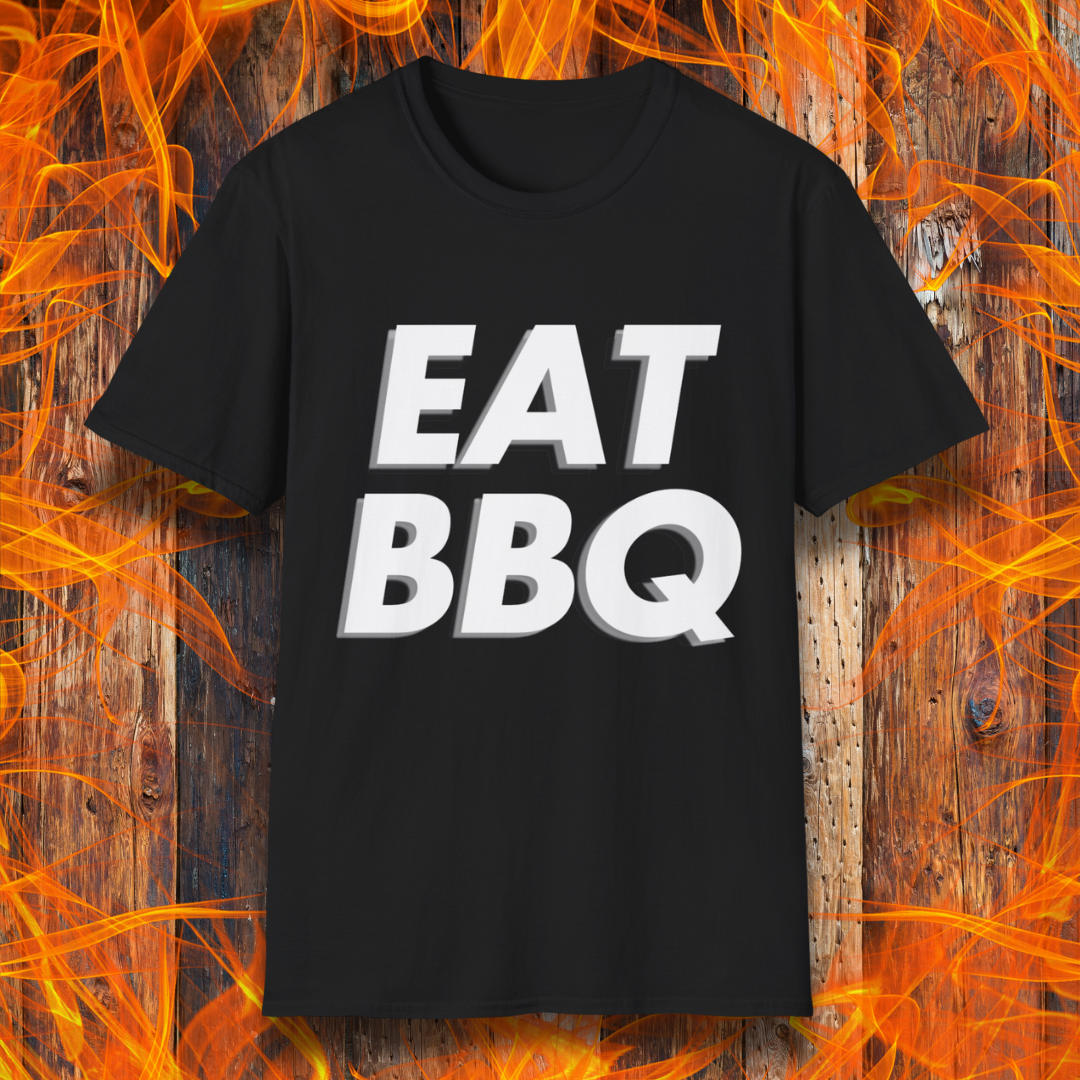 Black T-shirt featuring bold, blocky white text that reads "EAT BBQ" with a 3D effect. The shirt is displayed against a fiery wooden background, emphasizing the BBQ theme.