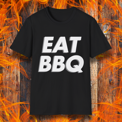 Black T-shirt featuring bold, blocky white text that reads "EAT BBQ" with a 3D effect. The shirt is displayed against a fiery wooden background, emphasizing the BBQ theme.