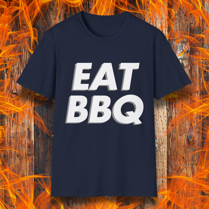 Navy T-shirt featuring bold, blocky white text that reads "EAT BBQ" with a 3D effect. The shirt is displayed against a fiery wooden background, emphasizing the BBQ theme.